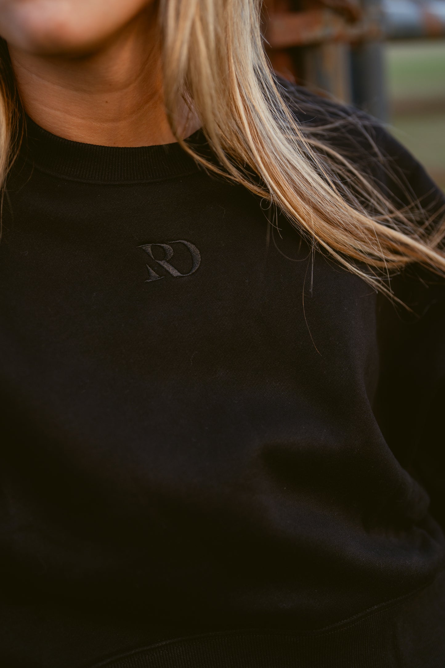 closeup of girl wearing cropped black western warmup hoodie Ranch Dress'n embroidered tone on tone RD