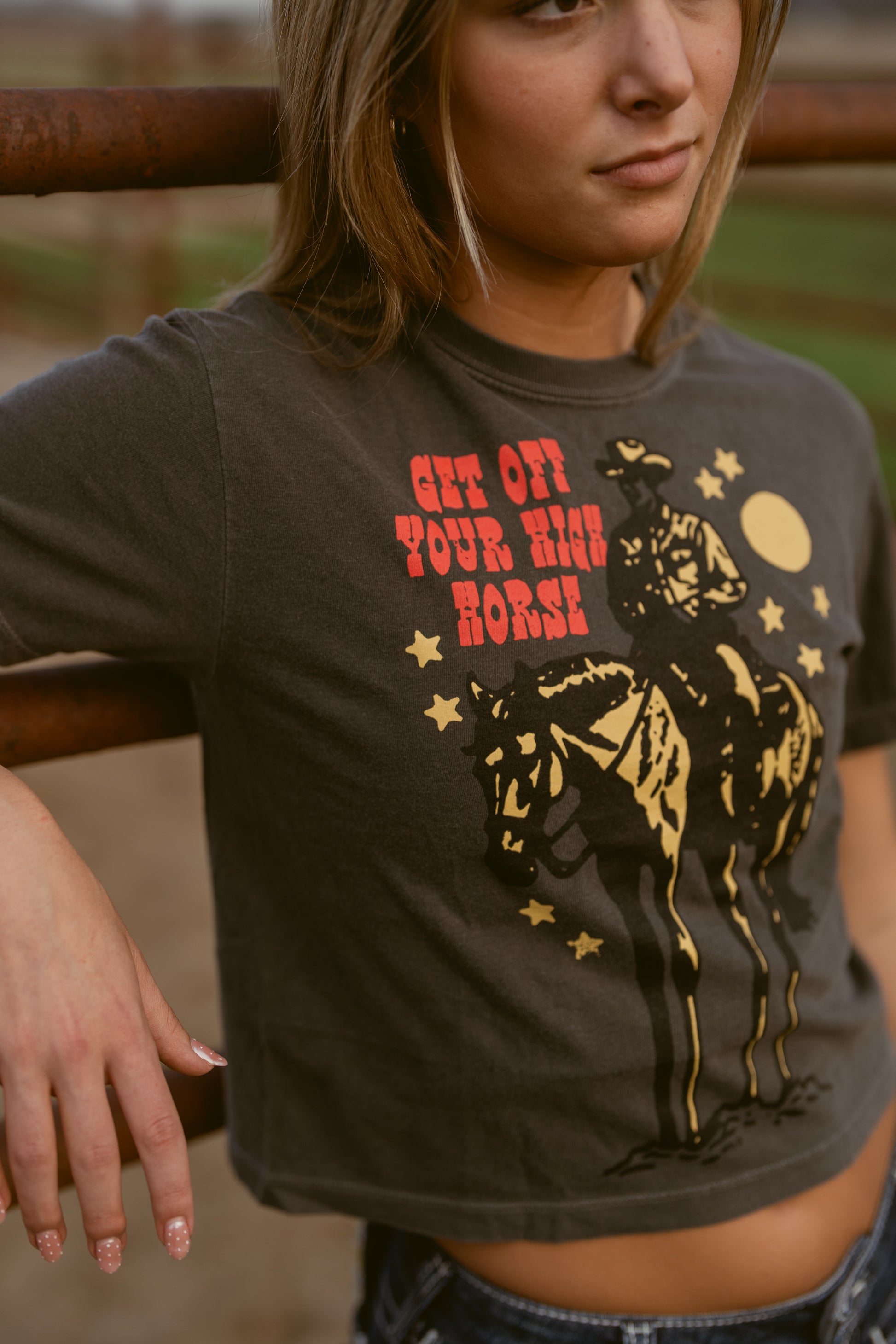 Woman wearing a t-shirt with a graphic design and text, standing outdoors.